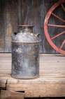 Still-life of old milk can and wagon wheel. Art Print